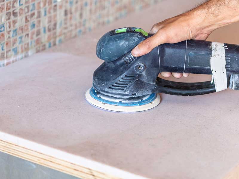 A worker is sanding a counter-top made from artificial stone. This process creates silica dust, which is hazardous to health if inhaled.